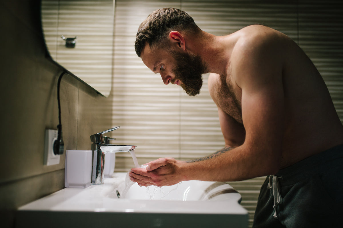 Man washing his hands in a bathroom sink with a mirror above.