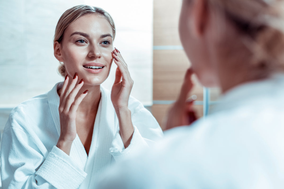 Woman in a white robe examining her face in a mirror